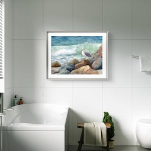 May include: A framed watercolor painting of a seagull perched on rocks near the ocean. The artwork features a crashing wave with shades of blue and green. The rocks are brown and gray, and the seagull has gray and white feathers.