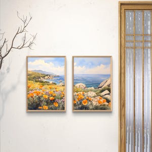 May include: Two framed watercolor paintings depicting coastal landscapes. The left painting shows a field of orange wildflowers with a rocky coastline and ocean in the background. The right painting shows a rocky coastline with the ocean in the background.