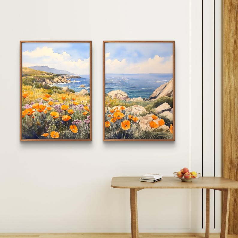 May include: Two framed watercolor paintings depicting a coastal landscape. The left painting shows a field of orange poppies in the foreground with a rocky coastline and blue ocean in the background. The right painting shows a close-up of the rocky coastline with the blue ocean in the background.