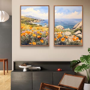 May include: Two framed watercolor paintings depicting a coastal landscape with orange wildflowers in the foreground and a blue ocean in the background. The paintings are hung on a wall above a dark grey cabinet.
