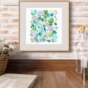 Puede incluir: Impresi&oacute;n art&iacute;stica en acuarela enmarcada con un dise&ntilde;o abstracto de formas redondeadas de colores en tonos azules, verdes y grises. La obra de arte se muestra en un marco de madera de color claro, sobre una pared de ladrillo.
