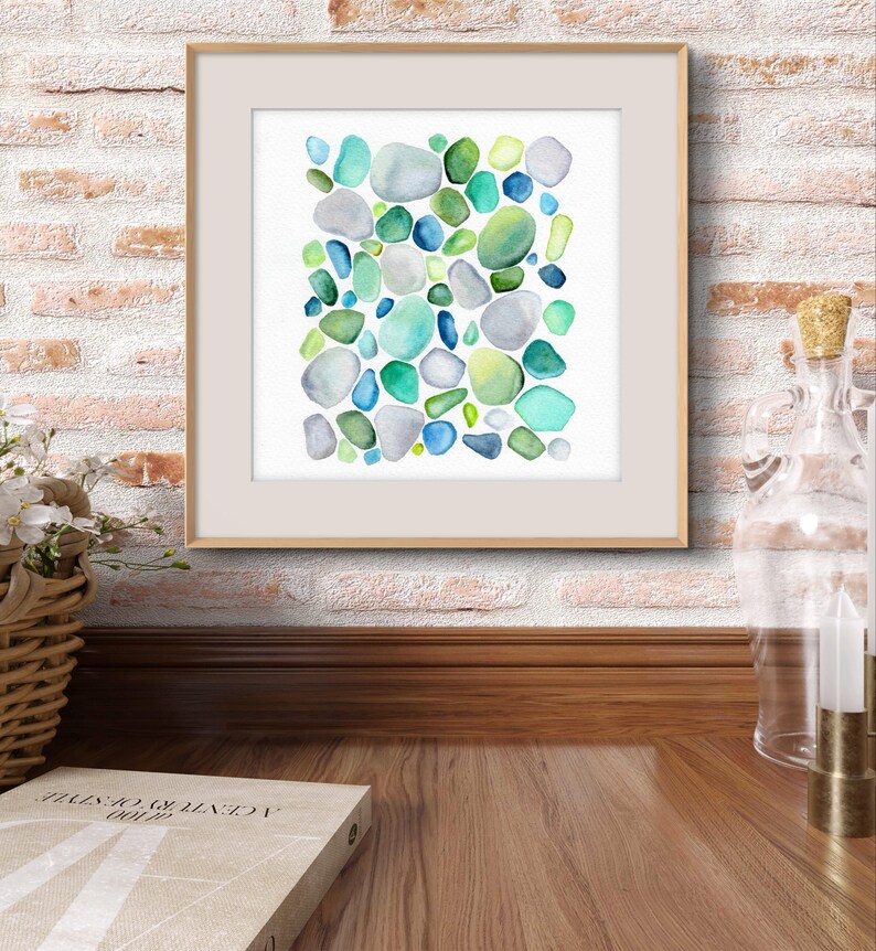 Puede incluir: Impresi&oacute;n art&iacute;stica en acuarela enmarcada con un dise&ntilde;o abstracto de formas redondeadas de colores en tonos azules, verdes y grises. La obra de arte se muestra en un marco de madera de color claro, sobre una pared de ladrillo.