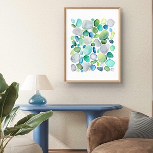 Puede incluir: Una impresi&oacute;n en acuarela enmarcada que presenta un dise&ntilde;o abstracto de formas redondeadas en tonos de azul, verde y gris. La obra de arte se exhibe en una pared de color neutro, agregando un toque de arte inspirado en la naturaleza al interior.