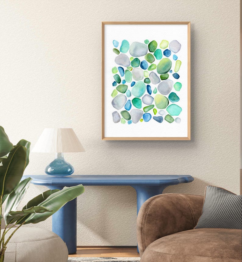 Puede incluir: Una impresi&oacute;n en acuarela enmarcada que presenta un dise&ntilde;o abstracto de formas redondeadas en tonos de azul, verde y gris. La obra de arte se exhibe en una pared de color neutro, agregando un toque de arte inspirado en la naturaleza al interior.