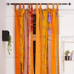 Può includere: Un set di tende patchwork arancioni, gialle e viola con un motivo floreale. Le tende sono realizzate con sari riciclati e sono appese a un'asta di metallo.