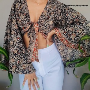 May include: A black and brown paisley print crop top with a tie front and long bell sleeves. The top is made of a lightweight fabric and has a relaxed fit.