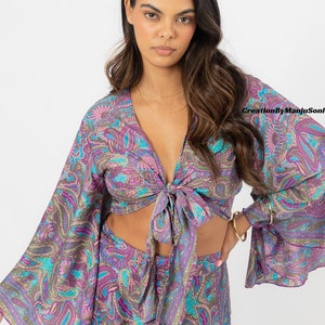 May include: A purple and blue paisley print crop top with long sleeves and a tie front. The top is made of a soft, flowing fabric and has a relaxed fit.