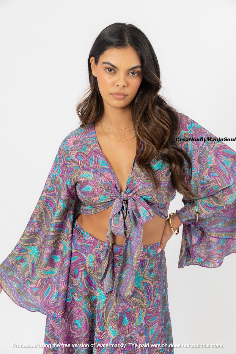 May include: A purple and blue paisley print crop top with long sleeves and a tie front. The top is made of a soft, flowing fabric and has a relaxed fit.