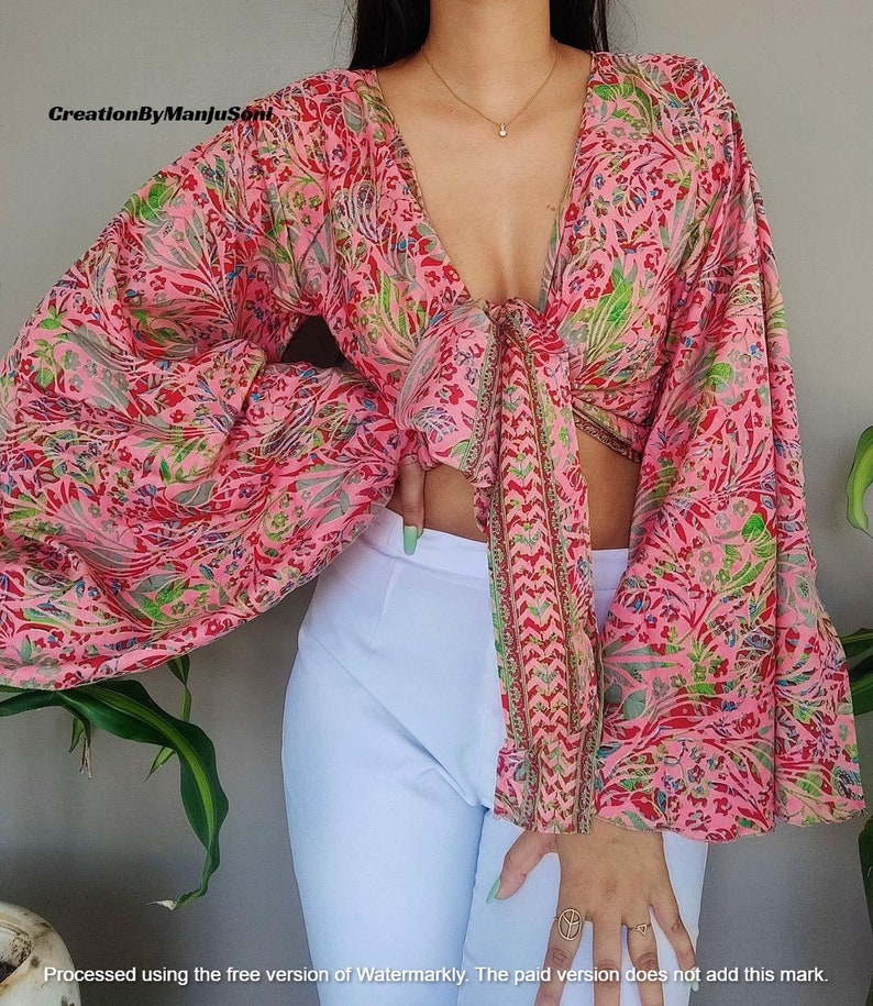 May include: A pink and green floral print crop top with long sleeves and a tie front. The sleeves are gathered at the shoulders and wrists.