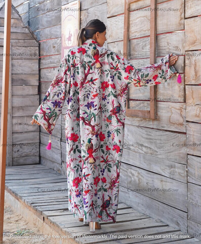 May include: A white long-sleeved robe with a floral print featuring colorful birds and flowers. The robe has a pink tassel on the sleeve.
