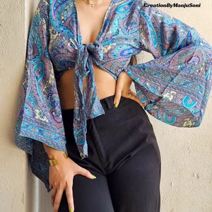 May include: A blue and purple paisley print crop top with long sleeves and a tie front. The sleeves are bell-shaped and the top is tied at the front.