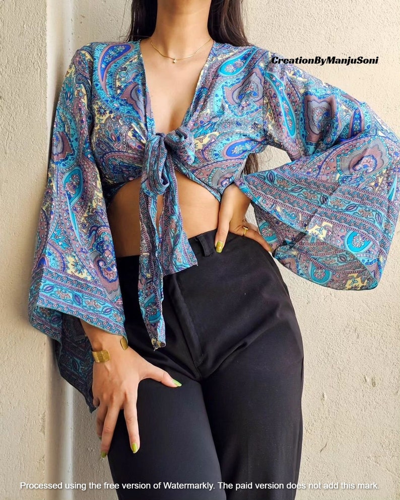 May include: A blue and purple paisley print crop top with long sleeves and a tie front. The sleeves are bell-shaped and the top is tied at the front.