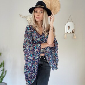 May include: A woman wearing a blue and floral print top with a black hat. The top has a loose fit and long sleeves. She is also wearing black jeans.