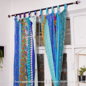 May include: A set of colorful patchwork curtains made from recycled saris. The curtains are hung on a wooden rod and feature a variety of blue, green, and orange patterns.