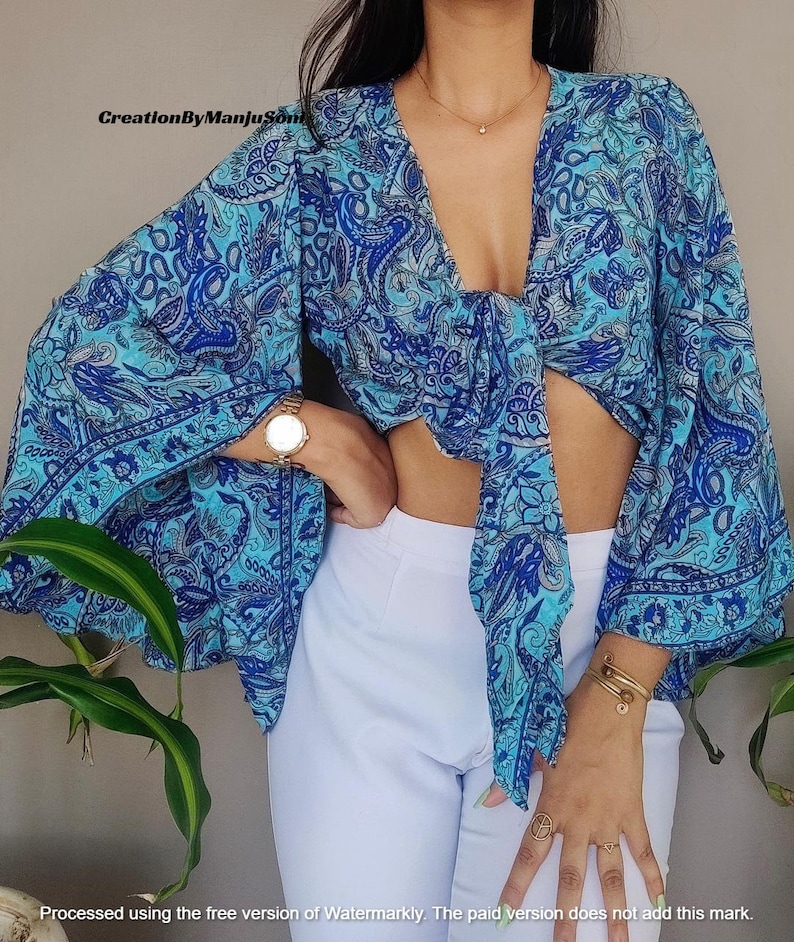 May include: A blue and white paisley print crop top with a tie front and long bell sleeves.