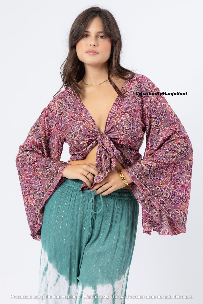 May include: A pink and purple paisley print top with long bell sleeves and a tie front. The top is cropped and has a deep V-neckline.