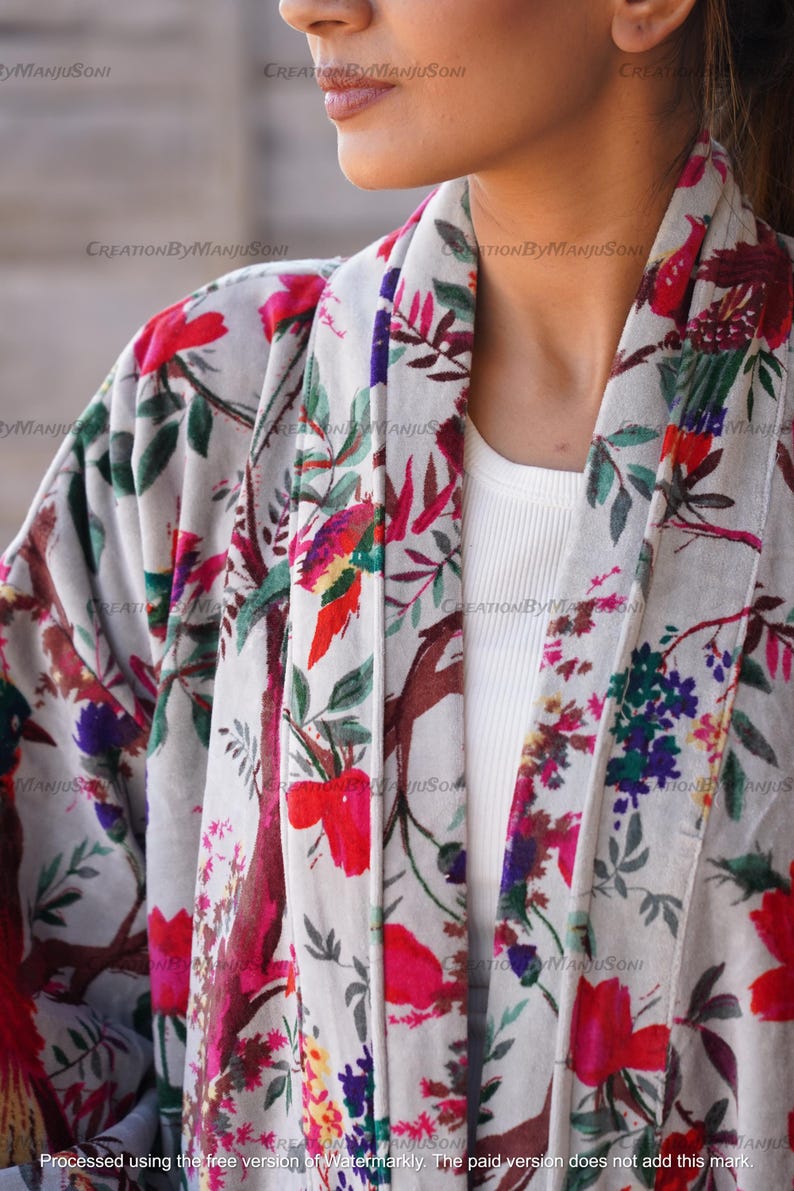 May include: A white kimono with a floral print featuring pink, red, green, and purple flowers. The kimono has a long sleeve and a wide collar.