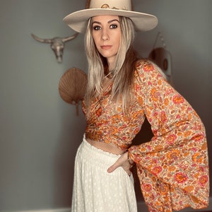 May include: A woman wearing a white hat with a brown and orange floral print top and a white skirt with eyelet detailing.