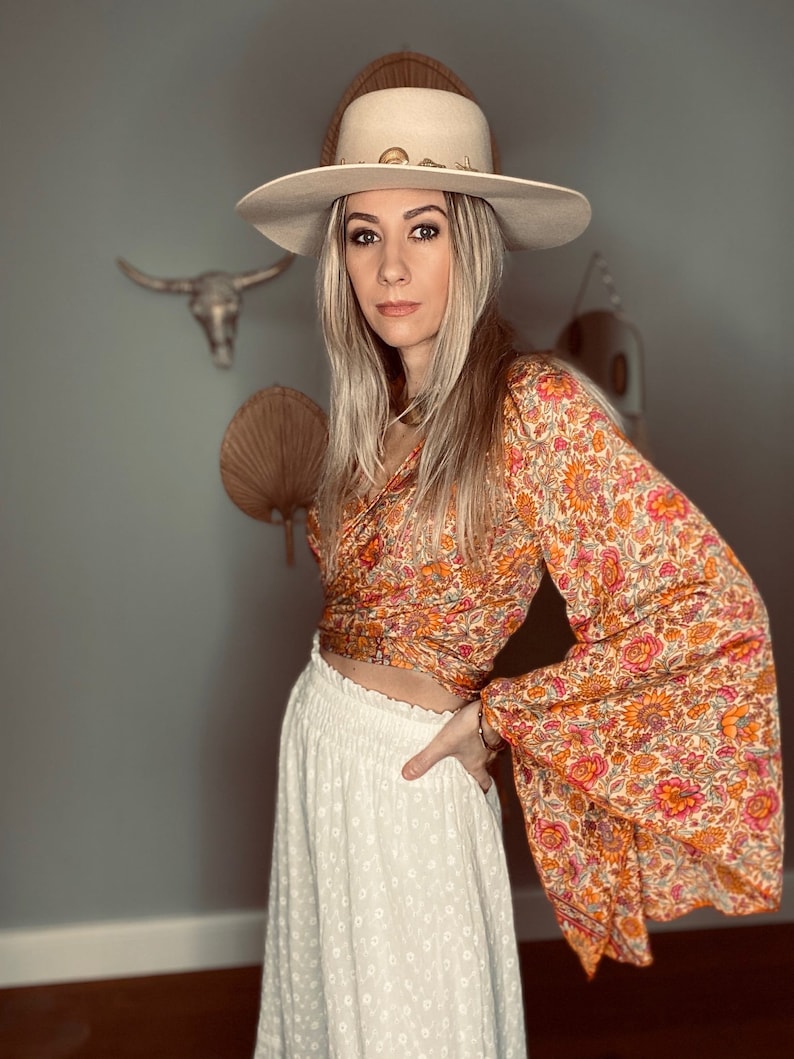 May include: A woman wearing a white hat with a brown and orange floral print top and a white skirt with eyelet detailing.