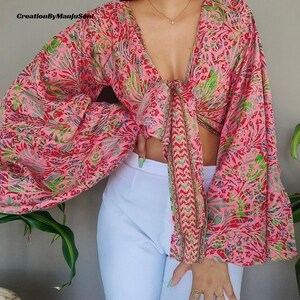 May include: A pink and green floral print crop top with long sleeves and a tie front. The sleeves are gathered at the shoulders and wrists.