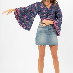 May include: A woman wearing a blue and purple floral print wrap top with long bell sleeves and a denim skirt.