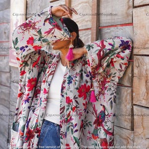 May include: A long-sleeved, white kimono with a floral and bird print. The kimono has a pink tassel on the left side and a pink tassel on the right side. The kimono is worn over a white t-shirt and blue jeans.