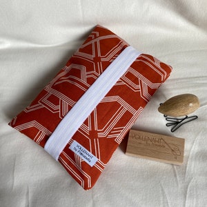 May include: A red and white geometric patterned fabric pouch with a white elastic band. The pouch has a label that reads "VOLLENAHT by Primabella".