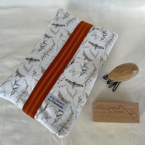 May include: A white fabric pouch with a brown and white butterfly print and orange stripes. The pouch has a label that reads "VOLLENAHT by Primabella".