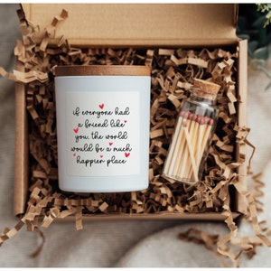 May include: A white candle with a wooden lid and a label that reads "if everyone had a friend like you, the world would be a much happier place". The candle is in a box with brown shredded paper and a small glass jar with matches.