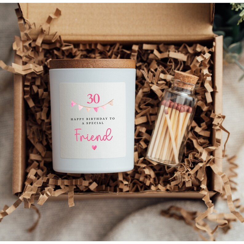 May include: A white candle with a wooden lid in a brown box with shredded paper. The candle has a label that says "30 Happy Birthday to a Special Friend" with pink hearts and bunting. A small glass jar with matches is also in the box.