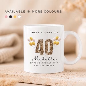 May include: A white ceramic mug featuring the text FORTY & FABULOUS, the number 40 in a leopard print pattern, the name Michelle, and the text HAPPY BIRTHDAY TO A SPECIAL SISTER, decorated with illustrations of small gold and pink balloons.