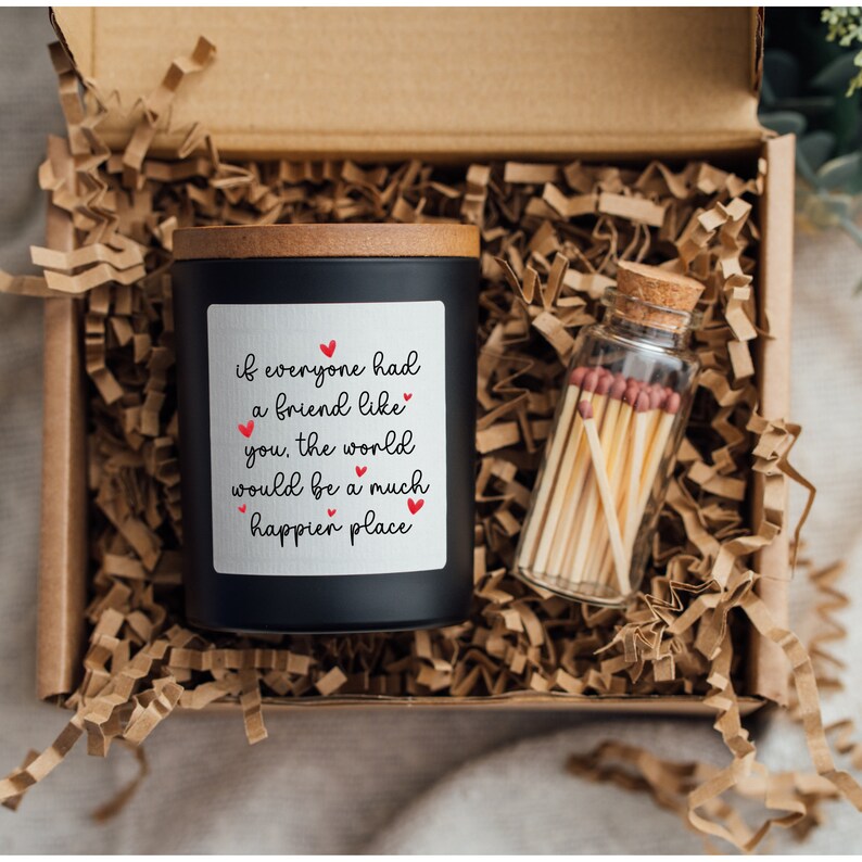 May include: A black candle with a wooden lid in a gift box with shredded paper. The candle has a white label with the text "if everyone had a friend like you, the world would be a much happier place" and red hearts. A small glass jar with matches is also in the box.