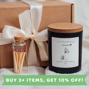 May include: A black candle with a wooden lid and a white label that reads "in loving memory of Auntie forever in our hearts". The candle is packaged in a brown box with a white satin ribbon. A small glass jar filled with matches is included.