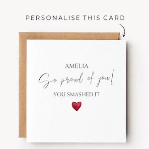 May include: A square white greeting card with a brown envelope featuring the text AMELIA, So proud of you!, and YOU SMASHED IT in black font, with a small red watercolour heart icon below the text and the words PERSONALISE THIS CARD above.