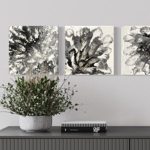 May include: Set of four black and white abstract paintings with a floral design. The paintings are square and are arranged in a row on a white wall.