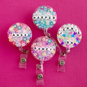 May include: Four colourful floral badge holders with clear retractable reels. The badge holders have the names "Harper", "Angie", "Romey", and "Jennie RN" spelled out in white letters.