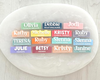 May include: A set of 14 colorful name tags with white text. The names include Olivia, Debbie, Jodi, Kathy, Michelle, Kristy, Ruby, Teresa, Sienna, Julie, Betsy, Kristy, Janine, and Sienna. The name tags are made of a smooth, glossy material.