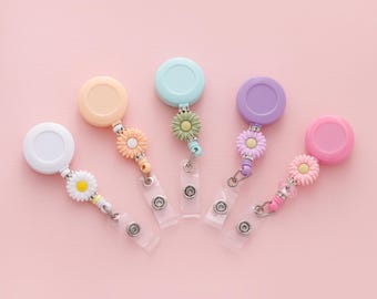 以下が含まれることがあります： デイジー型のチャームが付いた、伸縮式のバッジホルダー5個。ホルダーは、白、ピーチ、ライトブルー、パープル、ピンクなど、さまざまなパステルカラーです。
