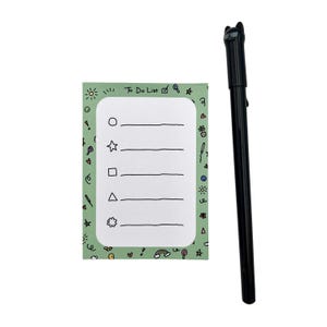 May include: A rectangular notepad with a light green border featuring small colorful doodles and the text To Do List at the top, containing five lines with geometric shapes for bullet points, paired with a black pen topped with a cat figure.