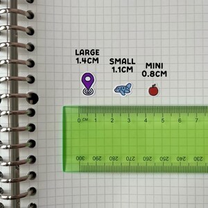 a green ruler placed on a grid of squares, with stickers indicating the size of objects in comparison to the ruler.