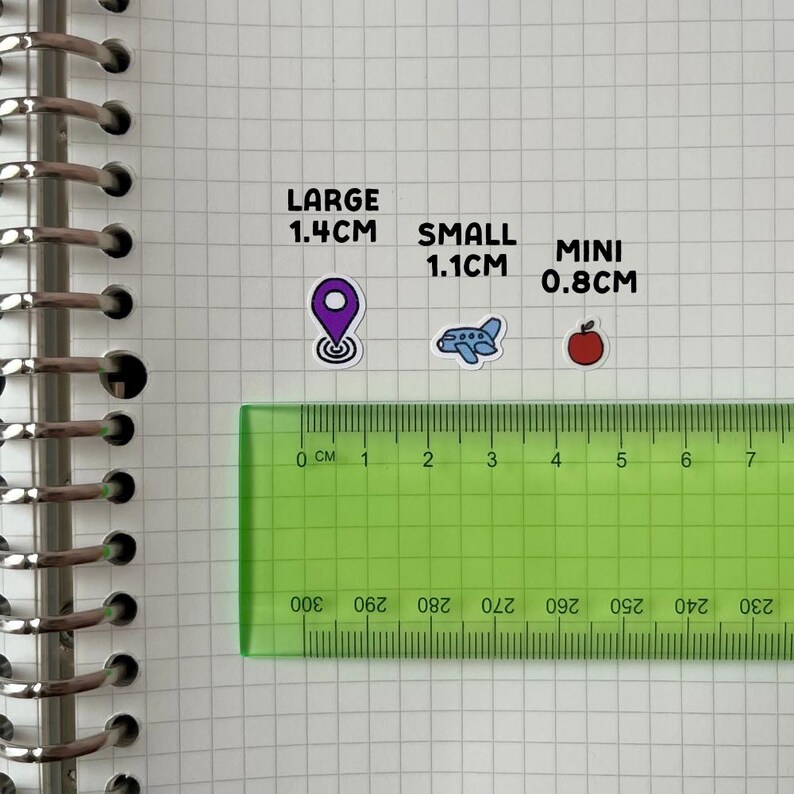a green ruler placed on a grid of squares, with stickers indicating the size of objects in comparison to the ruler.