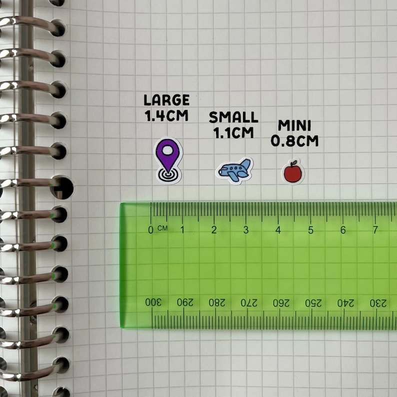 a green ruler placed on a grid of squares, with stickers indicating the size of objects in comparison to the ruler.