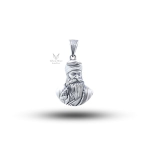 Może przedstawiać: Srebrny wisiorek przedstawiający szczegółowe popiersie mężczyzny z długą brodą i turbanem. Wisiorek ma pętlę na łańcuszek i naszyjnik z koralików. Obraz jest na białym tle z tekstem "Silver Bird Jewellery".