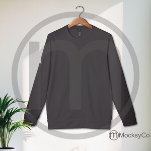 May include: A dark gray long-sleeved crew neck sweatshirt hanging on a wooden hanger against a white wall.