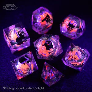 Puede incluir: Juego de siete dados de resina transparente con diseños de Halloween en naranja y negro. Cada dado presenta un diseño diferente, incluyendo un fantasma, una telaraña y un murciélago. Los dados están fotografiados bajo luz ultravioleta, con el texto "Umbrellas Co" y "*Photographed under UV light".