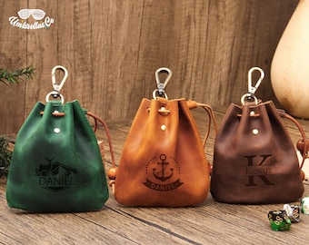 May include: Three personalized leather drawstring bags with different designs. The first bag is green with a deer and mountain design and the name "DANIEL". The second bag is brown with an anchor design and the name "DANIEL". The third bag is brown with a large "K" and the name "Kevin".