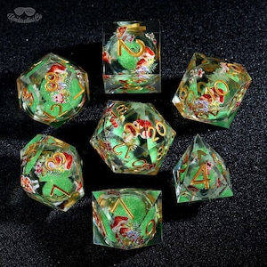 Può includere: Set di sette dadi poliedrici con esterno in resina trasparente, interno verde e numerazione dorata. Ogni dado presenta un design floreale e di funghi. I dadi sono disposti su una superficie scura.