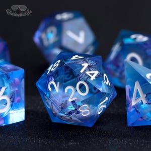 May include: A set of blue dice with white numbers and butterfly designs. The dice are made of clear plastic and have a iridescent finish.