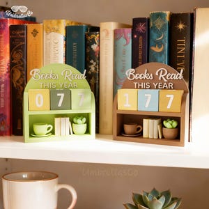 Op de afbeelding: Twee houten boektellers met de tekst "Books Read This Year". Eén is groen met het nummer "077", de andere is bruin met "177". Elk heeft een miniatuur kopje, boeken en een vetplant.