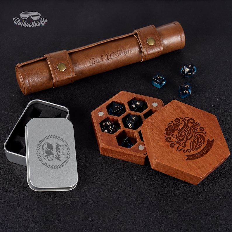May include: A wooden box with a hexagonal compartment for dice, with a lid that has a carved design and the name "Daniel". The box is open and shows black dice with gold numbers. A brown leather dice rolling tube with the name "Jack William" is also shown.